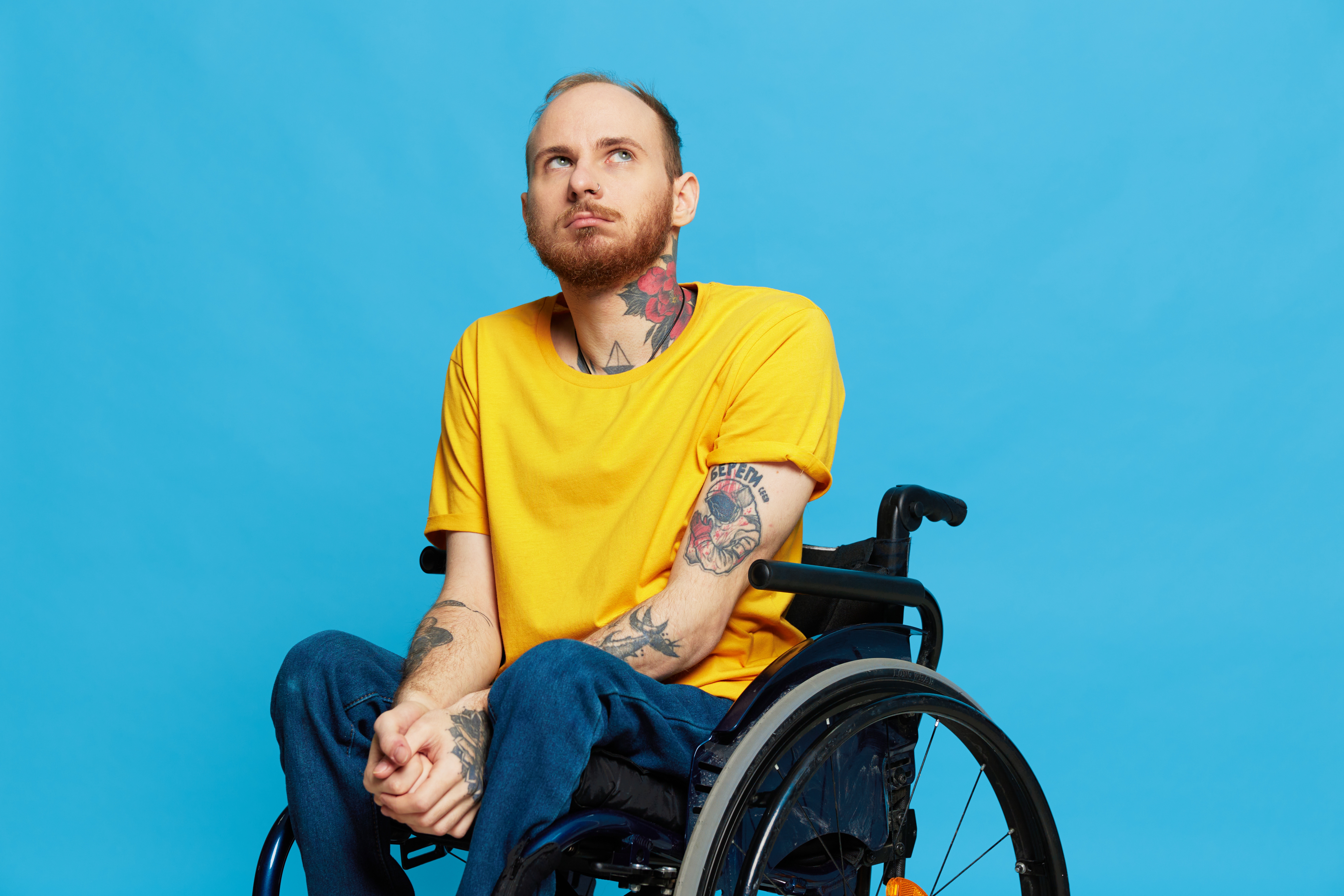 a man sits in a wheelchair in a t shirt on a blue background in the studio, the concept of a free barrier free environment for people with disabilities